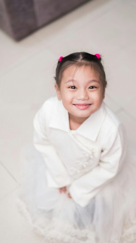 Cute Little Girl Smiling in White Outfit Mobile Phone Wallpaper