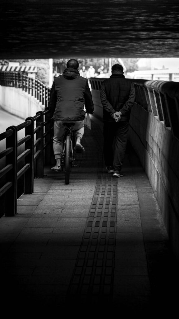 Black and White Street Photography of Two Men Walking Under Bridge Wallpaper