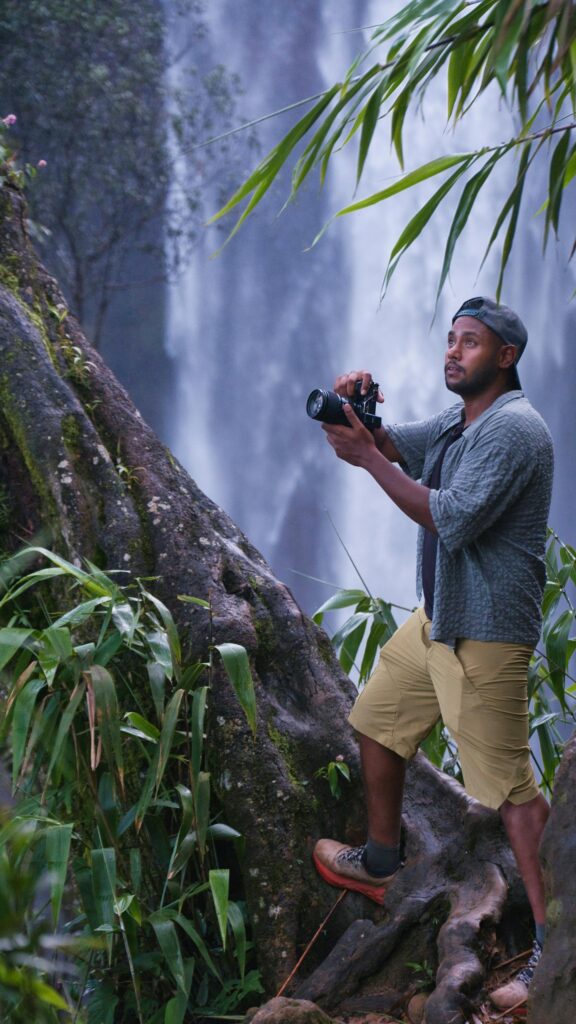 Adventurous Photographer Exploring Majestic Waterfall Mobile Wallpaper