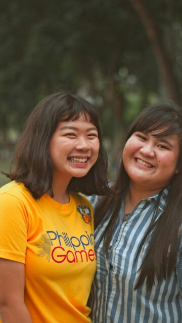 Two Smiling Asian Friends in Sunny Outdoor Setting Mobile Wallpaper