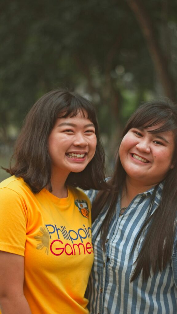 Two Smiling Asian Friends in Sunny Outdoor Setting Mobile Wallpaper