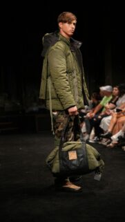 Military Fashion Runway Model with Green Puffer Bag Wallpaper