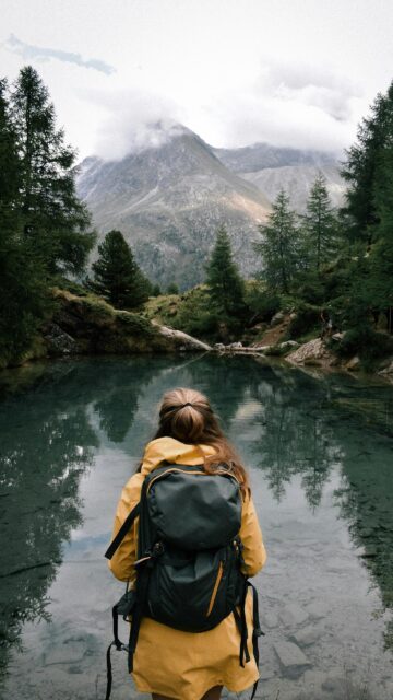 Woman Hiker Standing by Serene Mountain Lake Mobile Wallpaper