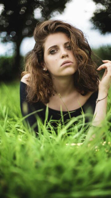 Stunning Portrait of a Young Woman in Lush Green Grass Phone Wallpaper