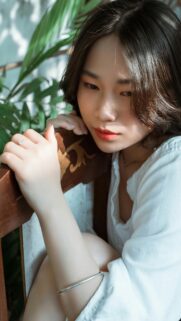 Sad Asian Girl Resting on Wooden Chair Portrait Phone Wallpaper