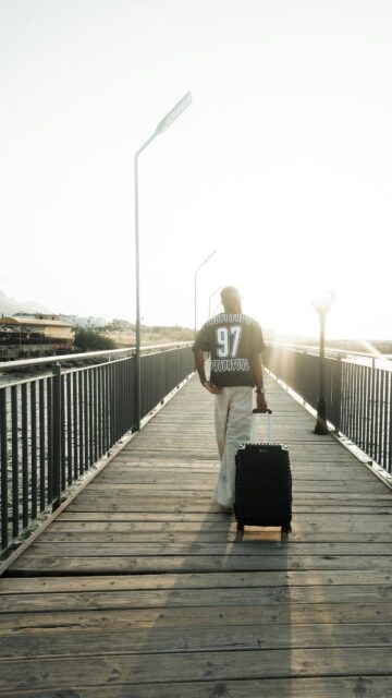 Man Walking on Sunny Wooden Pier with Suitcase Mobile Wallpaper