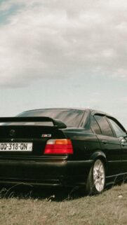 Black BMW E36 M3 Sedan in a Grassy Field Mobile Wallpaper
