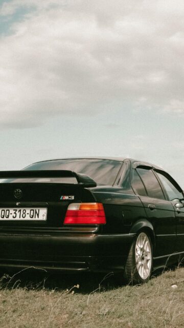 Black BMW E36 M3 Sedan in a Grassy Field Mobile Wallpaper