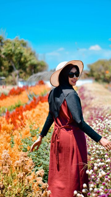 Elegant Woman in Hijab Walking Through a Sunlit Flower Field Wallpaper