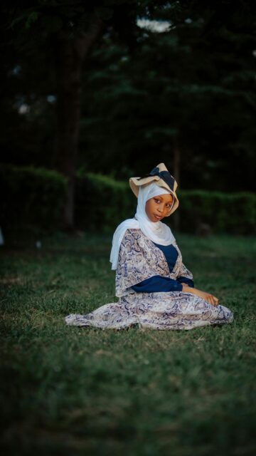 Woman Wearing Hijab and Summer Hat Sitting on Grass Wallpaper