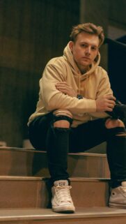 Young Man with Camera in Beige Hoodie Urban Style Phone Wallpaper