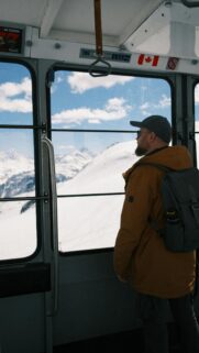 Man Looking Out at Snow Covered Mountains from Cable Car Wallpaper