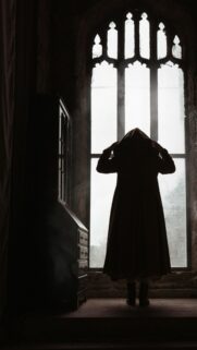 Mysterious Cloaked Figure in Gothic Window Silhouette Wallpaper