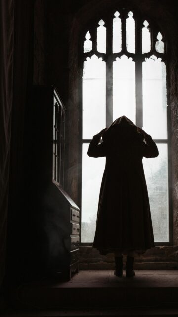 Mysterious Cloaked Figure in Gothic Window Silhouette Wallpaper