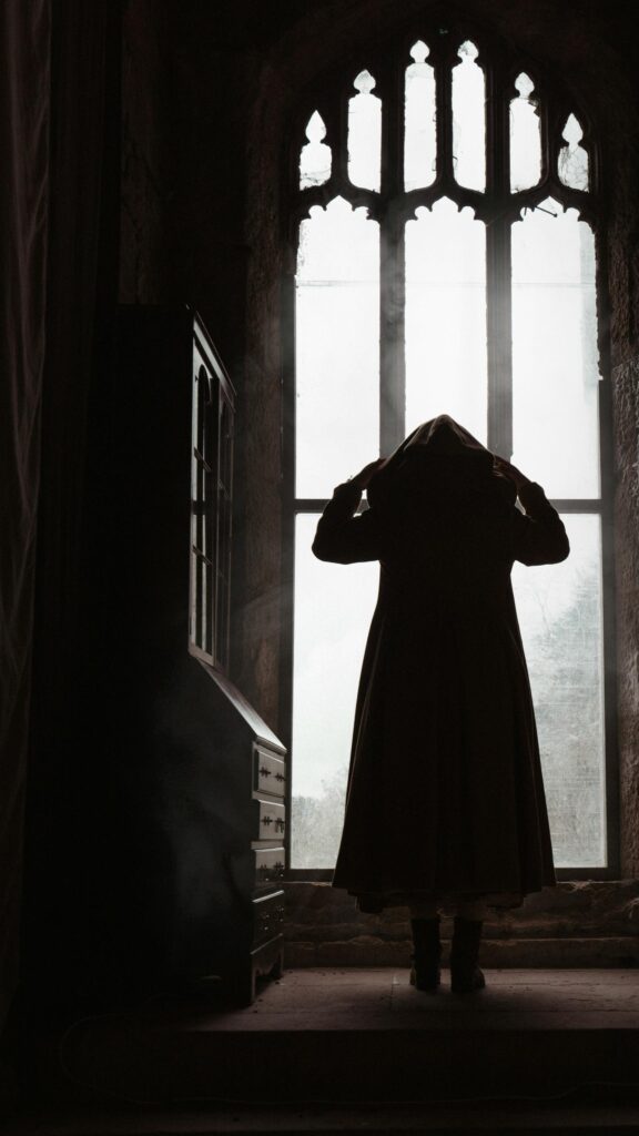 Mysterious Cloaked Figure in Gothic Window Silhouette Wallpaper