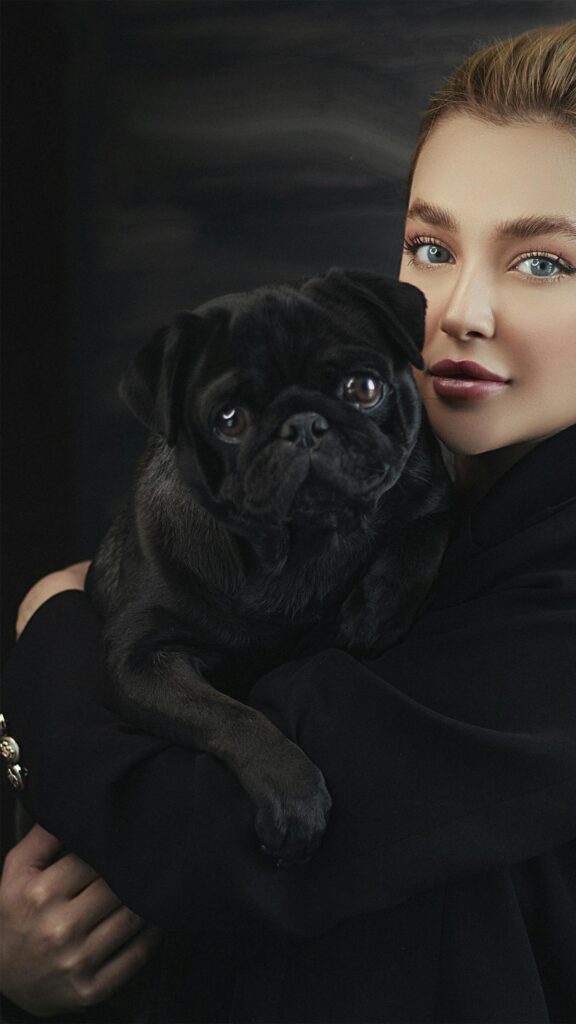 Stunning Portrait of a Woman Holding a Cute Black Pug Dog Wallpaper