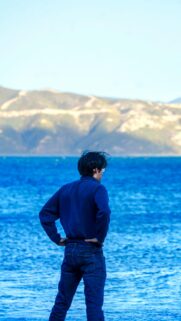 Man Standing by the Deep Blue Sea Facing Mountains Phone Wallpaper