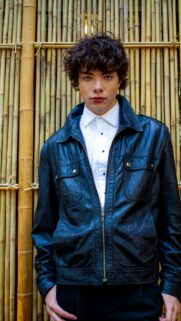 Young Man in Stylish Leather Jacket Against Bamboo Backdrop Wallpaper