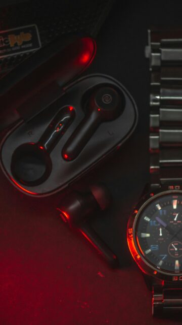 Sleek Black Earbuds and Metal Watch with Red Neon Lighting Mobile Wallpaper