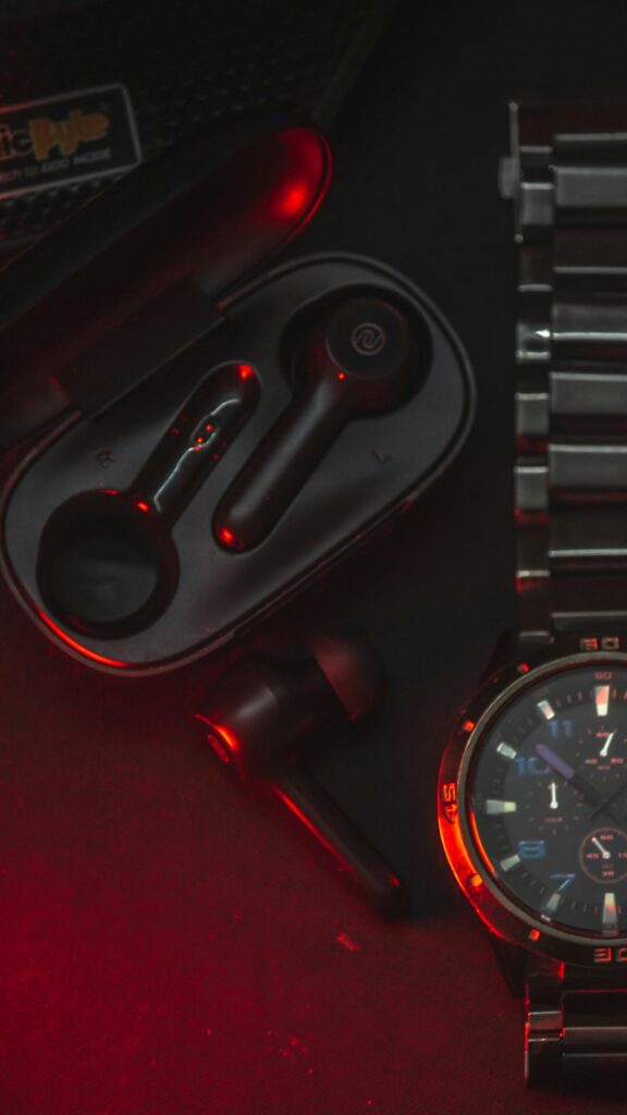 Sleek Black Earbuds and Metal Watch with Red Neon Lighting Mobile Wallpaper