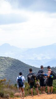 Four Hikers Standing on Mountain Peak Overlooking Valley View Wallpaper