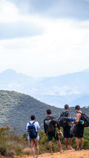 Four Hikers Standing on Mountain Peak Overlooking Valley View Wallpaper