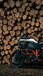 KTM Adventure Motorcycle Parked Against Rustic Wood Log Stack Wallpaper