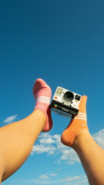 Playful Feet with Polaroid Camera Against Clear Blue Sky Wallpaper