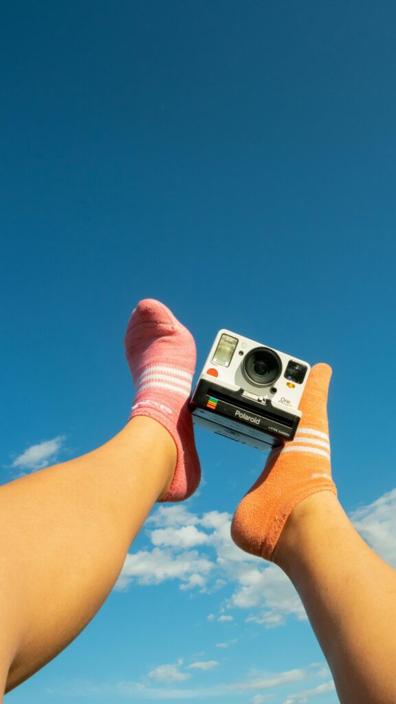 Playful Feet with Polaroid Camera Against Clear Blue Sky Wallpaper