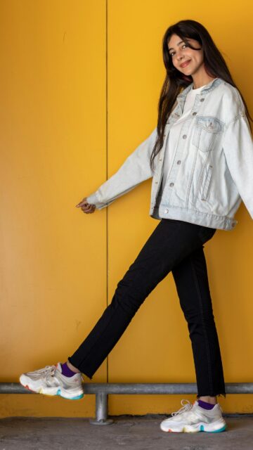 Young Stylish Woman Walking Along Yellow Wall Phone Wallpaper