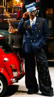 Stylish Man in Safety Pin Suit Standing Beside Vintage Red Mini Car Wallpaper