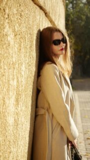 Elegant Woman in Beige Coat Against Golden Wall Phone Wallpaper