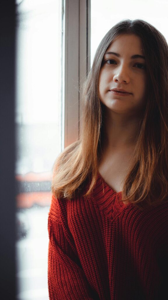 Stunning Young Woman in Red Sweater by Window Mobile Wallpaper