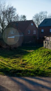 Sunlit Suburban Brick House and Rolling Green Field Wallpaper