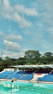 Sunny Stadium Swimming Pool with Vibrant Blue Seats Wallpaper