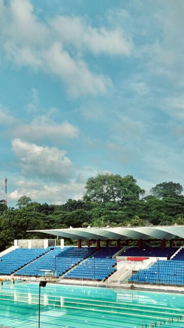 Sunny Stadium Swimming Pool with Vibrant Blue Seats Wallpaper
