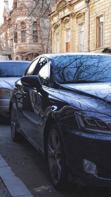 Sleek Dark Luxury Sedan Parked on Historic City Street Mobile Wallpaper
