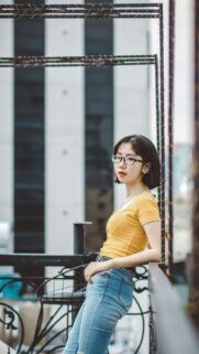 Stylish Asian Woman in Yellow Top Leaning on Railing Mobile Wallpaper