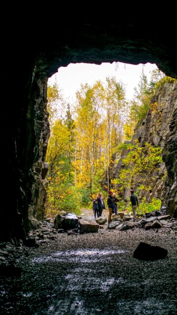 Group of Hikers Exploring an Autumn Stone Tunnel Cave Wallpaper