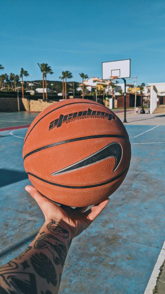 Close-up Basketball Held in Hand on Sunny Outdoor Court Wallpaper