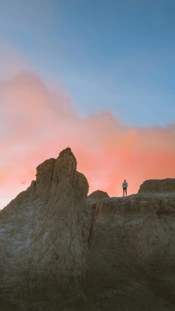 Solo Hiker Standing on Rocky Badlands Cliff at Sunset Wallpaper