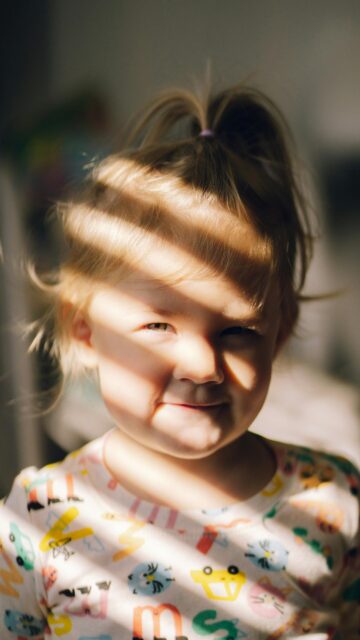 Adorable Toddler Girl with Sunbeam Shadows Portrait Phone Wallpaper