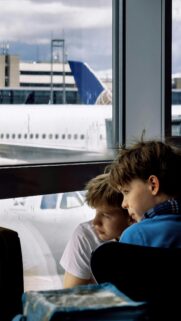 Two Boys Looking Out Airport Window at Plane Phone Wallpaper