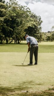 Elderly Golfer Focusing on Putt on Sunny Green Golf Course Wallpaper