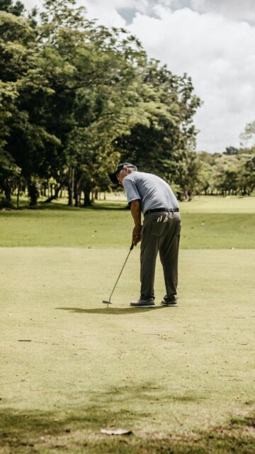 Elderly Golfer Focusing on Putt on Sunny Green Golf Course Wallpaper
