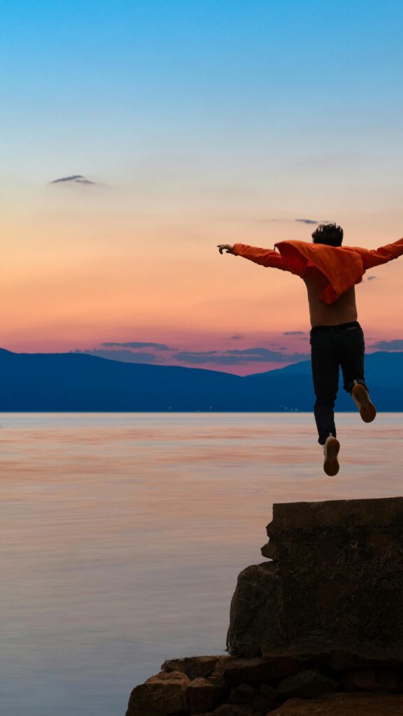 Man Jumping into Lake at Sunset Adventure Phone Wallpaper