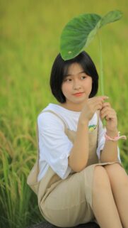 Cute Asian Girl Holding Large Leaf in Golden Rice Field Phone Wallpaper