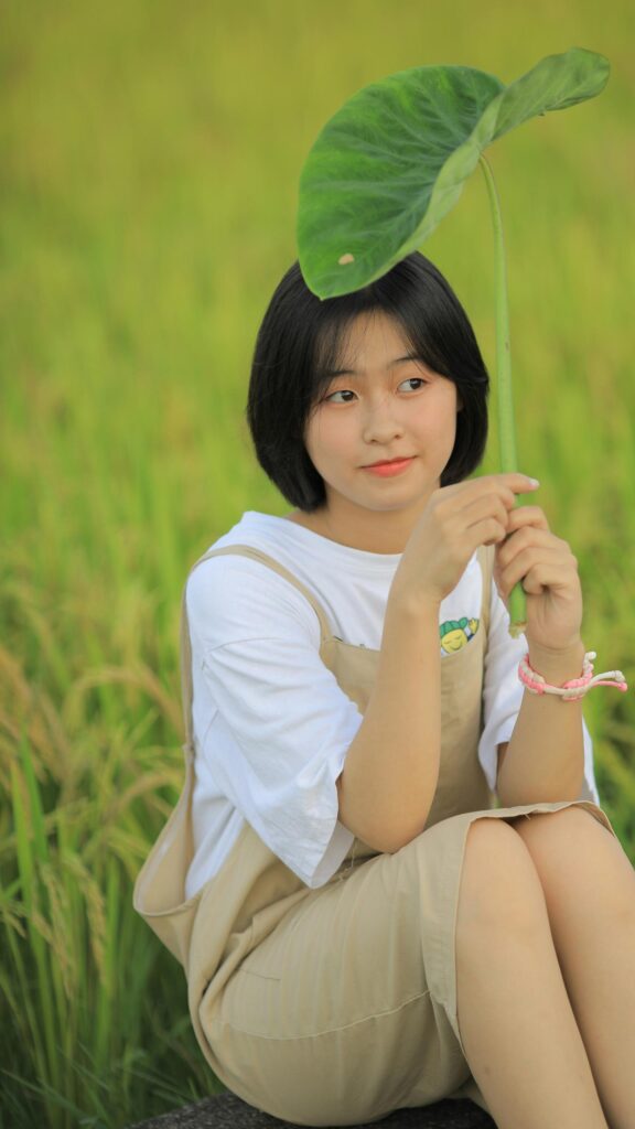 Cute Asian Girl Holding Large Leaf in Golden Rice Field Phone Wallpaper