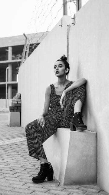 Stylish Woman in Polka Dot Jumpsuit Posing by Concrete Wall Wallpaper