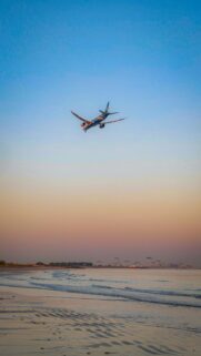Stunning Airplane Landing Over Peaceful Beach at Sunset Phone Wallpaper